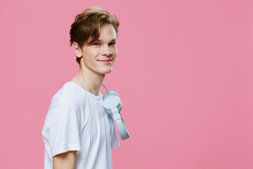 beautiful young man in a white T-shirt on a pink background with headphones around his neck smiling cutely at the camera