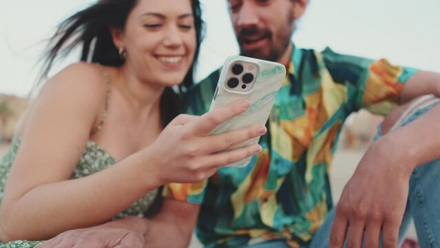 Close-up of young woman's hand holding mobile phone. Young couple using smartphone while sitting on the beach