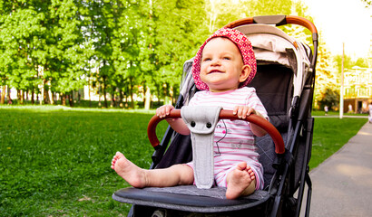 baby in a stroller in a green summer park. smiling baby in a hat