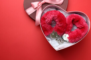 Gift box with furry handcuffs on red background, top view. Space for text