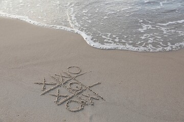 Tic tac toe game drawn on sand near sea, space for text