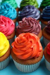 Many delicious colorful cupcakes on light blue background, closeup