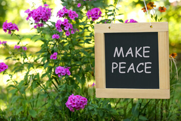 Chalkboard with phrase Make Peace near phlox flowers outdoors
