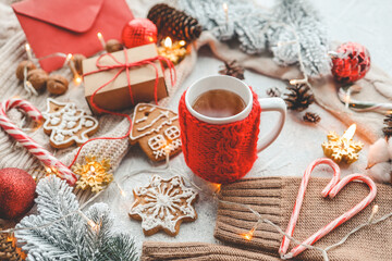 A cup of tea with a knitted red decoration, gingerbread, candy, candles and a garland. Christmas atmosphere at home