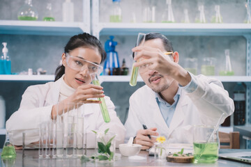 Two research people are comparing and discuss information about substance with tube in their hands at cosmetic lab. They are happy in their research.