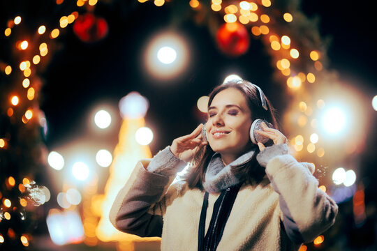 
Happy Woman Listening to Carols Outdoors on Christmas Eve. Lady enjoying xmas playlist on her portable device

