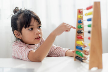 A young cute Asian girl is using the abacus with colored beads to learn how to count at home