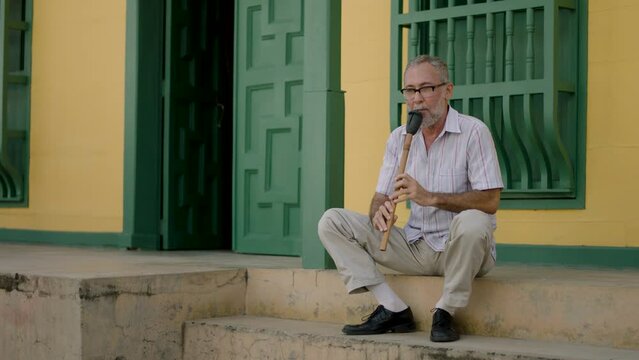 A musician plays the flute on the entrance of his house.