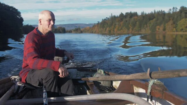 A mature man driving rowboat with outboard engine surrounded by Autumn colours