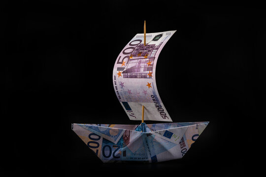 A paper boat made of paper with the image of euro banknotes of various denominations with a sail from a banknote of 500 euros on a black background