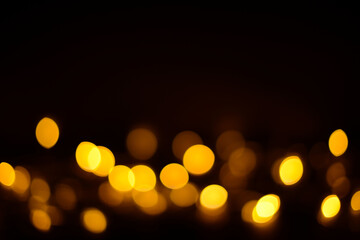 Fototapeta premium Golden bokeh on a black background. Festive glowing glitter background with blurred lights of garlands for party, new year, birthday, anniversary background, holidays