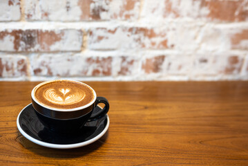 Cup of coffee on a wooden table against a brick wall