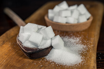 Close up of white sugar cubes on a wooden spoon, on the kitchen table. Preparation of cakes and sweets in the kitchen.