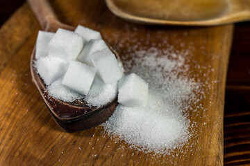 Close up of white sugar cubes on a wooden spoon, on the kitchen table. Preparation of cakes and sweets in the kitchen.