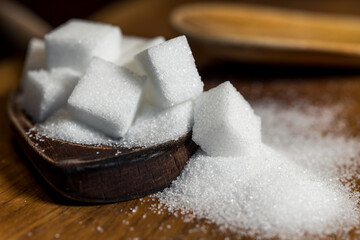 Close up of white sugar cubes on a wooden spoon, on the kitchen table. Preparation of cakes and sweets in the kitchen.