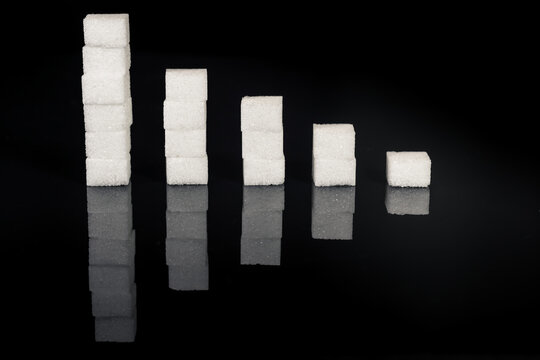 Falling Blood Sugar Levels. Sugar Cubes Put In A Falling Sugar Level Graph. Sugar Cubes On A Black Glossy Background.