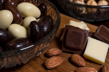 Almond, milk and white chocolate, and chocolate-coated almonds in three types; dark chocolate, milk chocolate, white chocolate. High-quality sweets in Belgian chocolate, arranged on a wooden board.