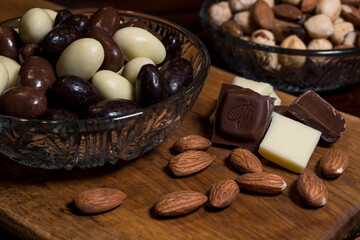 Almond, milk and white chocolate, and chocolate-coated almonds in three types; dark chocolate, milk chocolate, white chocolate. High-quality sweets in Belgian chocolate, arranged on a wooden board.