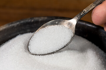 White sugar on a tablespoon, taken from a sugar bowl. Metal spoon with sugar.