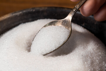 White sugar on a tablespoon, taken from a sugar bowl. Metal spoon with sugar.