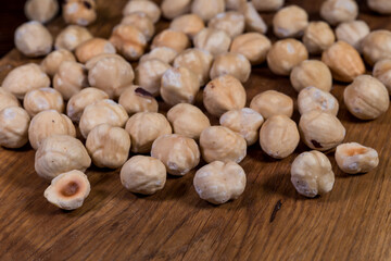 Hazelnut - edible fruit of various species of shrubs of the genus hazel (Corylus). Roasted hazelnuts. Whole hazelnuts and walnut halves, scattered on a wooden board.