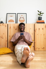 Young smiling black man relaxing at home using cellphone texting a friend. Vertical image.