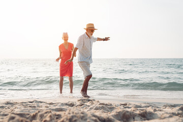 Happy senior couple in love walking and dancing together on the beach having fun in a sunny day, activity after retirement in vacations and summer.
