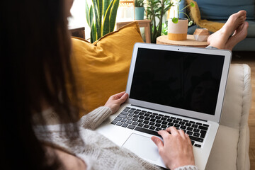 POV of young caucasian woman using laptop relaxing at home lying on couch.