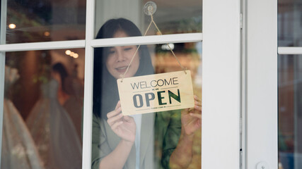 Woman hanging open sign on door, Store owner turning open sign broad through the door glass and...