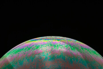 Rainbow soap bubble on a black background close-up.