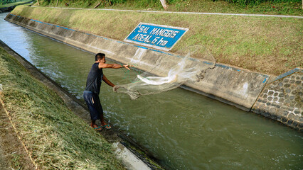 Magelang, Indonesia - October 29th 2022 : A man is catching fish in the river using a net