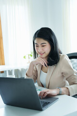 Portrait of a thoughtful Asian businesswoman looking at financial statements and making marketing plans using a computer on her desk