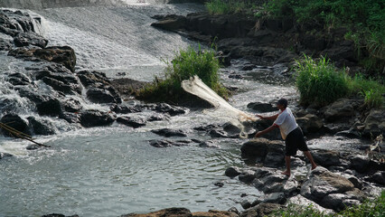 Magelang, Indonesia - October 29th 2022 : A man is catching fish in the river using a net