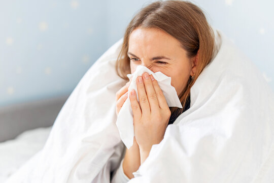 Sick woman sneezing holding tissue paper napkin sitting on couch at home