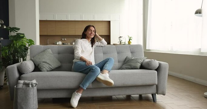 Pensive dreamy woman resting on sofa looking into distance feels happy, enjoy day off, spending carefree weekend alone at modern cozy own or rented dwelling. Tenancy, independence, daydreams concept