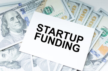 Startup Funding inscription on a card on the background of dollar bills on the table