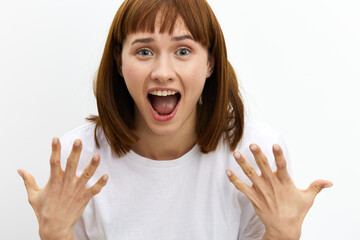 a beautiful, attractive woman stands on a white background in a white T-shirt and screams loudly with delight, actively gesticulating with her hands and eyes wide open
