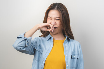 Portrait of pretty brunette hair, disgust smell bad strong asian young woman, girl hand squeezing, covering nose with fingers, expression face disgusting, dislike odor isolated on white background. - obrazy, fototapety, plakaty