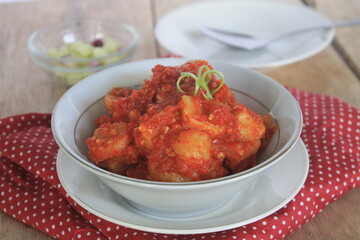 Sambal fried meatballs in a white bowl on a table covered with red polka dot cloth

