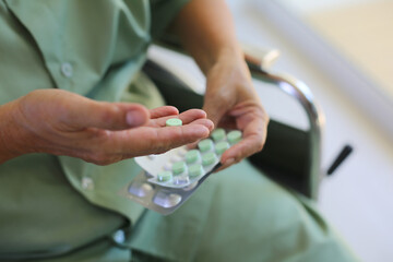 Closeup on Medicine Pills on hand of patient sitting on wheelchair.