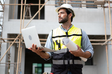 CAucasian Man Worker in a construction site. Architecture engineering holding a laptop on building...