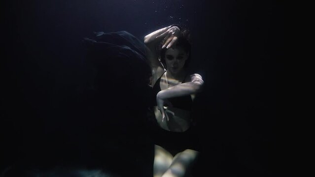 beautiful girl in a black dress dancing underwater on a dark background