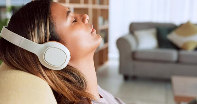 Woman, headphones and relax listening to music on living room sofa with eyes closed at home. Female enjoying calm audio track with wireless headset relaxing in comfort on couch at the house indoors