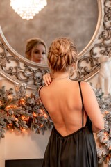 Portrait of a wealthy mature woman with evening make-up and hairstyle posing in a black dress on the background of the Christmas room. Luxurious lifestyle. Christmas holidays concept