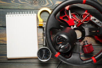 Sport car tuning accessories and blank page notepad on the wooden workbench flat lay background....