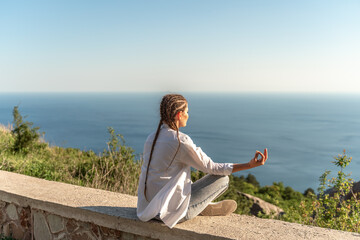 Naklejka na ściany i meble Profile of a woman doing yoga in the top of a cliff in the mountain. Woman meditates in yoga asana Padmasana