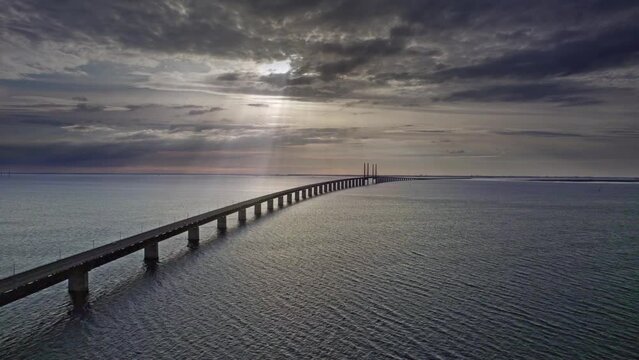 Aerial view high angle of the colorful sunset, the sun's rays breaking through the clouds over the sea and reflected on the calm waves. At the bridge over the &Ouml;resund strait between Sweden and Denmark