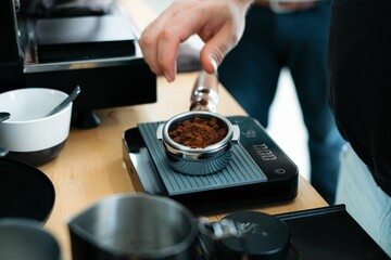 Human hand measuring freshly grounded coffee on scale before putting into machine