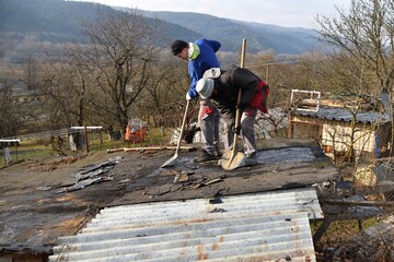 Roof workers remove pieces of cardboard roof manually with shovel