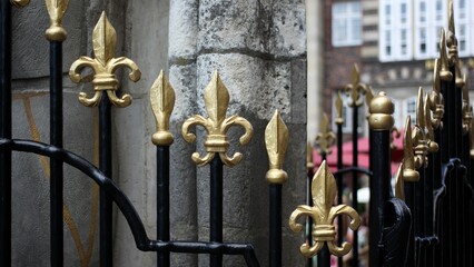 Closeup of a metal black fence with golden tips in front of the stone building